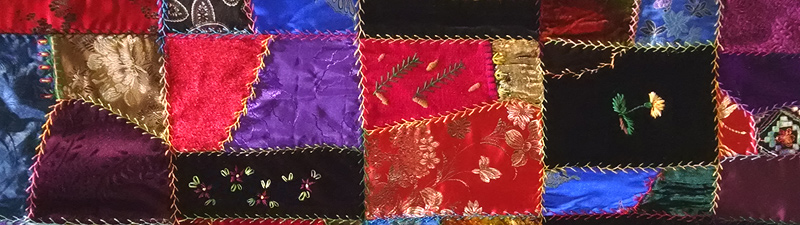 A section of a hand-made crazy quilt, made of random-shaped pieces of velvet and satin with embroidered seams and small embroidered motifs such as flowers and butterflies.