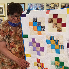 Narda LeCadre holds up a quilt she made, featuring colorful blocks on a white background