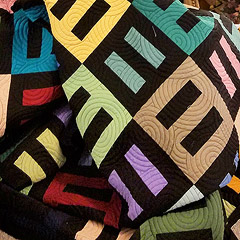 A quilt with alternating squares of black bars against a solid-color background, or colored bars against a black background