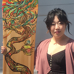 Aron Rook holds a snowboard that she decorated: it has a stylized image of a twisted tree in jewel-tone colors