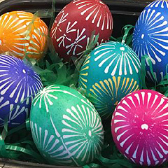 Several colorful decorated Easter eggs nestle in crinkly plastic Easter-basket grass. Each egg is a single bright color with white starburst designs.