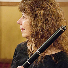 Lesl Harker in profile, watching someone. She holds her flute at an angle; only the top several inches are visible in the photo. She has a mass of wavy auburn hair.