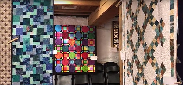 AAQG hosted a quilt display at Fort Hunter Barn in 2021, showcasing quilts made by members.
    >> This still shot from the video shows three large quilts plus bits of two others.  In the center is one in jewel tones and black that looks like stained glass.