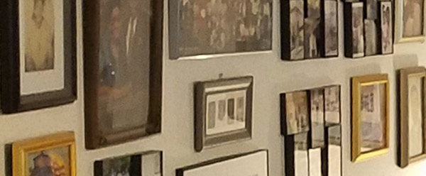 Numerous framed photographs hang close together on the wall.  This photo is taken at an angle, so the images in the frames aren’t visible.