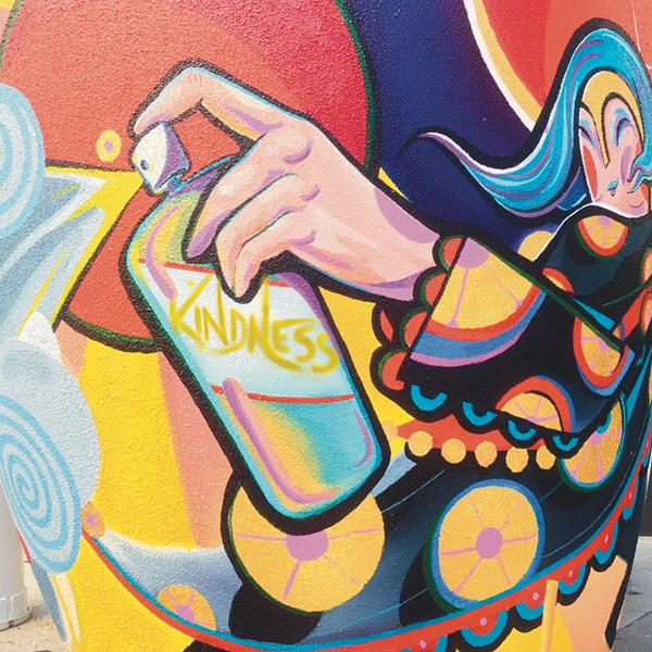 Another of Aron’s murals suggests painting the world with kindness.
>> A stylized woman holds a spray-can labeled ‘KINDNESS’, and she is spraying it around.