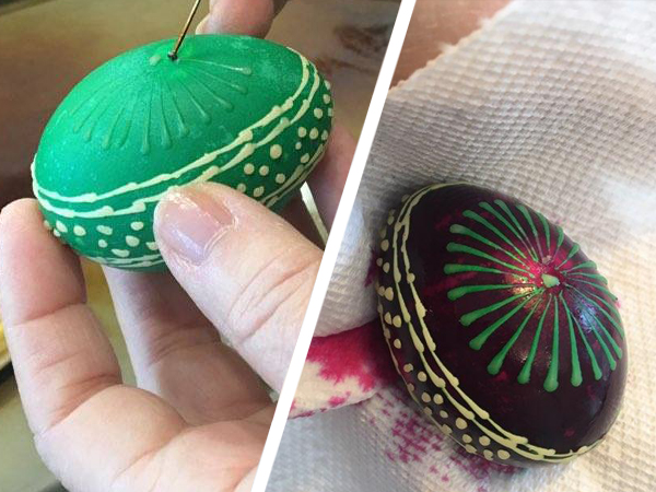 On the right side of this image, we see the completed multicolored egg: it is very dark purple/black, with a green pinwheel design and a band of dots and lines that circles the egg vertically. On the left, we see the same egg in mid-process: it has been dyed green, and there’s wax over the belt pattern. Barbara is creating the pinwheel pattern by applying wax on the empty face of the egg.
