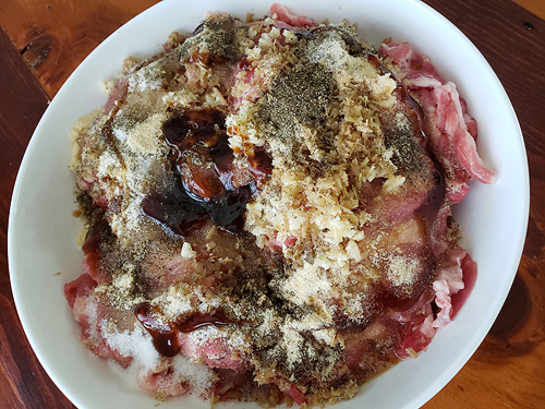 The white bowl of raw pork now has all the marinade ingredients added. They are all sitting on top, not yet mixed in.