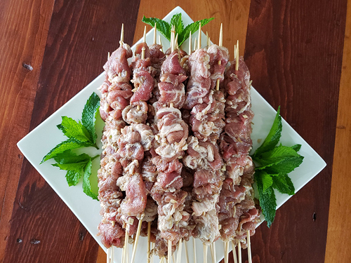 The marinated pork strips have been threaded zigzag-wise onto skewers. More than a dozen of these, each with several inches of meat on the skewer, are stacked diagonally on a square white plate, with mint sprigs placed artfully on the empty corners.
