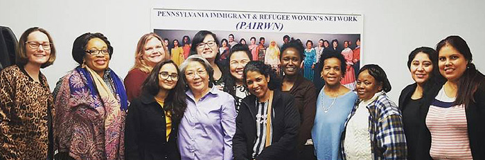 Ho-Thanh stands with a dozen women of the Pennsylvania Immigrant & Refugee Women’s Network. Most appear to be middle-aged; most are women of color; all are nicely dressed and smiling, looking happy, standing close together, side by side.