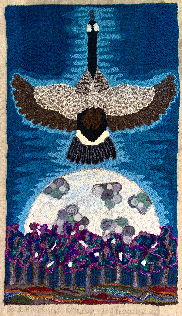Goose Moon Rising shows a Canada goose in flight, seen from the top with outstretched neck reaching up to the top of the rug and wings stretching out to both side edges. Below the goose is a huge grayish-white moon rising from a line of trees done in jewel tones of purple, teal and blue. The moon has ‘craters’ of darker gray and green. The goose’s back, wings and tail are shaded and detailed with appropriate colors. The background is an evening sky, light blue near the goose and fading to darker blue near the edges of the rug. The finished rug appears to be about two feet wide and four feet tall.