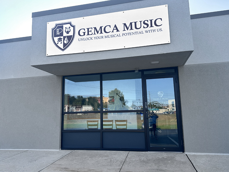 A store front in a strip mall, with a large sign over the door: GEMCA MUSIC - Unlock your musical potential with us. It looks about 20 feet across, with large plate-glass windows.