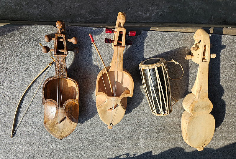 The instrument at right is barely begun; its bulbous outer shape has been carved, but it is still a solid chunk of wood.  The one in the middle has been hollowed out, and strings are in place. The instrument at left is nearly complete, with stained wood and strings.