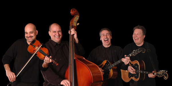 The four members of Sviraj, wearing black and photographed against a black background, playing their instruments and grinning. These are all white men who appear to be in their 50s, and who also appear to be having a great time together. At far left, Mike Furjanic playing fiddle, looking down and slightly to his right. Beside him, Chris Radanovic playing an upright bass. Next is Lenny Tepsich, playing celo, with his mouth open as if he’s laughing out loud. At far right is Danilo Yanich, also with a big grin and his eyes squinted almost shut with merriment.